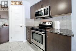 Kitchen featuring dark wood-finish cabinetry, granite-style countertops, stainless steel appliances, and a subway tile backsplash - 