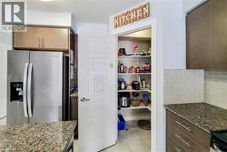 Kitchen featuring a walk-in pantry, stainless steel refrigerator, dark wood-finish cabinetry, and granite countertops - 
