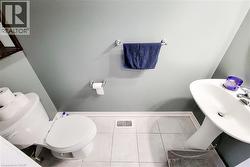 Bathroom featuring a white pedestal sink, toilet, light gray walls, white floor tiles, and white baseboards - 