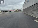 Expansive asphalt parking lot with clearly marked yellow parking lines, featuring a building with a gray brick lower facade and a corrugated metal upper facade with rectangular windows - 44 Ditton Drive Unit# 3, Hamilton, ON 
