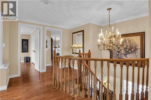 Upper landing featuring wood-finish flooring, a brass multi-tier chandelier with ceiling medallion, and a wood banister with traditional balusters - 228 Michener Crescent, Kitchener, ON - Indoor Photo Showing Other Room