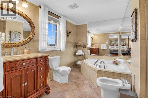 Built-in corner soaking tub with tile surround, paired with a custom wood vanity featuring an oval mirror and contemporary fixtures - 228 Michener Crescent, Kitchener, ON - Indoor Photo Showing Bathroom