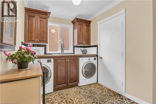 Dedicated laundry area featuring wood-finish cabinetry, a white sliding window, and a utility sink with a high-arc faucet - 228 Michener Crescent, Kitchener, ON - Indoor Photo Showing Laundry Room