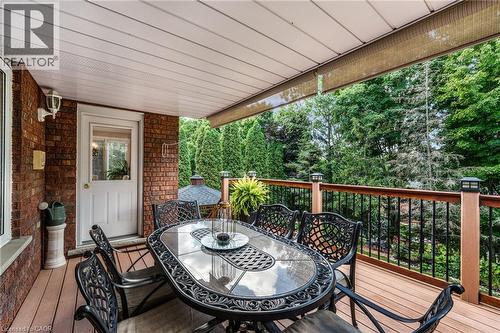 Covered wood-finish deck featuring a brick exterior wall, white entry door, and dark wood-finish railing with black balusters - 228 Michener Crescent, Kitchener, ON - Outdoor With Deck Patio Veranda With Exterior