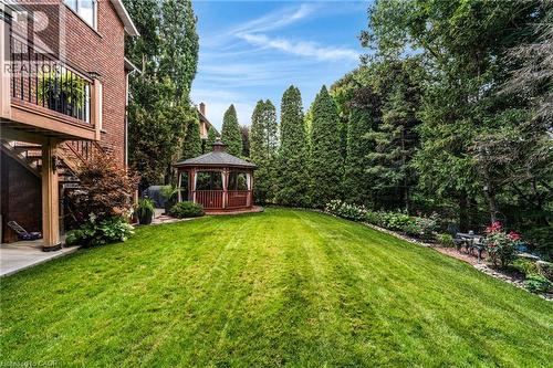 Expansive backyard featuring a manicured lawn, a wooden gazebo with white privacy curtains, mature evergreen trees, and a terraced garden with established plantings - 228 Michener Crescent, Kitchener, ON - Outdoor