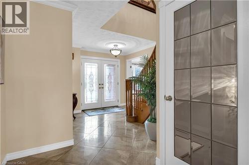 Entryway featuring double doors with decorative glass panels, a circular ceiling medallion with a flush mount light fixture, large format tile flooring, and a wooden staircase with a matching railing - 228 Michener Crescent, Kitchener, ON - Indoor Photo Showing Other Room