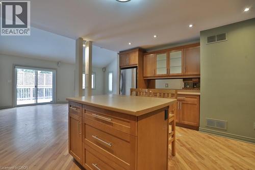 Kitchen island with light-toned countertop and wood-finish cabinetry, stainless steel refrigerator, and wood-finish flooring - 7 Gibson Place Unit# 21, St. Catharines, ON - Indoor Photo Showing Kitchen