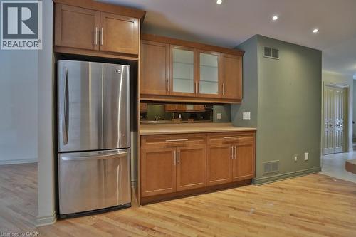 Built-in wet bar featuring wood-finish cabinetry, a stainless steel refrigerator, mirrored backsplash, and recessed lighting - 7 Gibson Place Unit# 21, St. Catharines, ON - Indoor Photo Showing Kitchen
