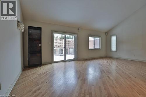 Spacious room featuring wood-finish flooring, vaulted ceiling, built-in display cabinet, and sliding glass doors opening to an exterior deck - 7 Gibson Place Unit# 21, St. Catharines, ON - Indoor Photo Showing Other Room