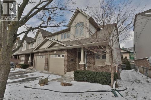 Brick and siding exterior featuring a covered front porch with white columns, two garage doors with upper window inserts, and dormer windows - 7 Gibson Place Unit# 21, St. Catharines, ON - Outdoor
