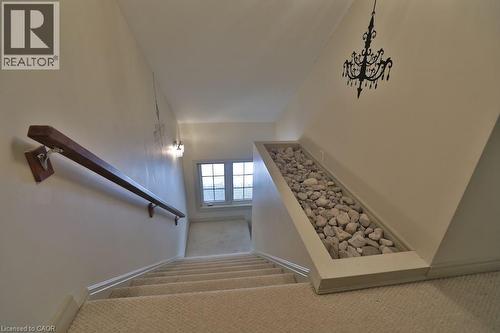 Carpeted staircase featuring a wood handrail, recessed wall lighting, a decorative wall decal, and a unique built-in rock garden under the stairwell - 7 Gibson Place Unit# 21, St. Catharines, ON - Indoor Photo Showing Other Room