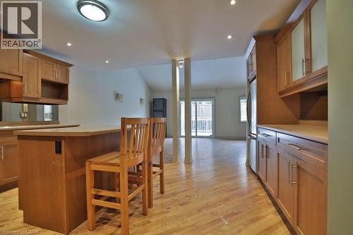 Kitchen and living area featuring wood-finish flooring, light wood cabinetry with frosted glass accents, and a built-in breakfast bar - 7 Gibson Place Unit# 21, St. Catharines, ON - Indoor Photo Showing Kitchen