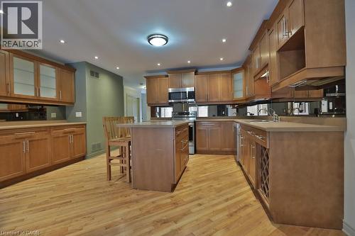 Kitchen featuring wood-finish flooring, recessed lighting, wood cabinetry with glass-front accents, a central island, and stainless steel appliances - 7 Gibson Place Unit# 21, St. Catharines, ON - Indoor Photo Showing Kitchen