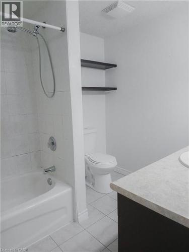 Bathroom featuring a white tub with tiled surround, a toilet, a dark wood-finish vanity with light-toned countertop, and light-toned floor tiling - 569 Activa Avenue, Kitchener, ON - Indoor Photo Showing Bathroom