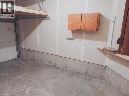 Garage interior featuring a concrete floor, finished walls, overhead wood-finish shelving, and a wall-mounted wood-finish storage cabinet - 569 Activa Avenue, Kitchener, ON - Indoor Photo Showing Garage