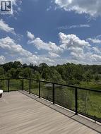 Spacious outdoor deck featuring composite wood-finish flooring, a contemporary glass and metal railing, and expansive tree canopy scenery - 