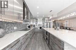 Kitchen featuring wall chimney exhaust hood, modern cabinets, gray cabinets, stainless steel fridge, and black electric stovetop - 