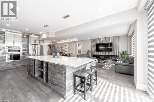 Kitchen featuring modern cabinets, a breakfast bar, stainless steel refrigerator with ice dispenser, a tiled fireplace, and light wood finished floors - 477 Blair Creek Drive, Kitchener, ON - Indoor