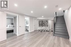 Finished below grade area featuring visible vents, recessed lighting, light wood-style flooring, baseboards, and stairway - 