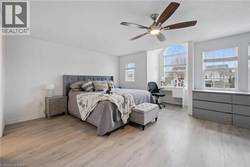 Expansive room featuring light wood-finish flooring, multiple windows including an arched top window, a built-in desk, and a ceiling fan with integrated lighting - 11 Patton Drive, Cambridge, ON - Indoor Photo Showing Bedroom