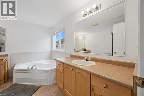 Bathroom featuring a corner soaking tub with tile surround, a double-pane window, and a vanity with a laminate countertop, integrated sink, and wood-finish cabinetry - 11 Patton Drive, Cambridge, ON - Indoor Photo Showing Bathroom