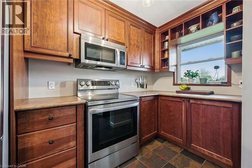 Kitchen featuring wood cabinetry, stainless steel appliances, a window with shelving, solid surface countertops, and tile flooring - 154 Oriole Street, Waterloo, ON - Indoor Photo Showing Kitchen
