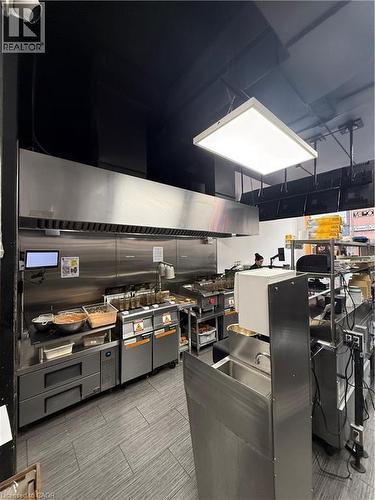 Commercial kitchen featuring a large stainless steel exhaust hood and a suspended rectangular light fixture - 85 King Street W, Kitchener, ON 