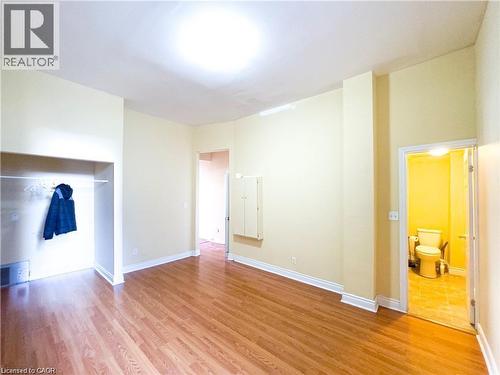 Spacious interior room featuring wood-finish flooring, light-toned wall paint, and white baseboards - 85 King Street W, Kitchener, ON 