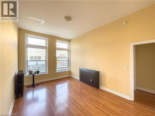 Living area featuring expansive windows, wood-finish flooring, and a classic cast iron radiator - 85 King Street W, Kitchener, ON 
