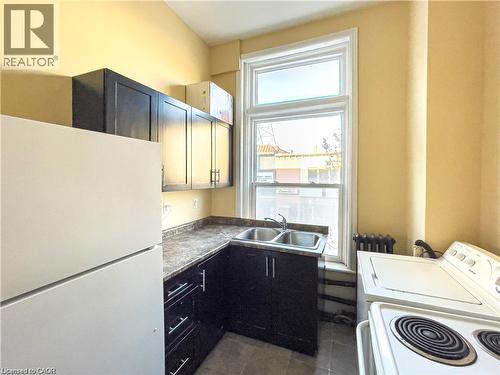 Kitchen featuring dark wood-finish cabinetry, a double basin stainless steel sink, and a light-colored countertop - 85 King Street W, Kitchener, ON 