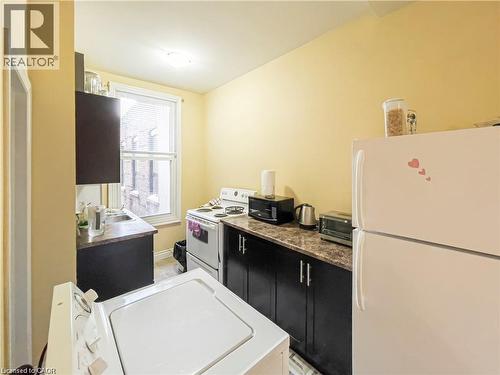 Compact kitchen featuring a white top-load washing machine, white range, and a white refrigerator - 85 King Street W, Kitchener, ON 