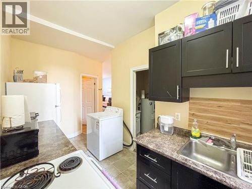 Compact kitchen area featuring a white refrigerator, dark cabinetry with silver-tone pulls, a stainless steel sink, wood-finish backsplash, and vinyl tile flooring - 85 King Street W, Kitchener, ON 