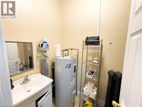 Compact utility area featuring a water heater, a white vanity with an integrated sink, and an exposed cast iron radiator - 85 King Street W, Kitchener, ON 