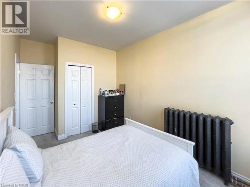 Room featuring a built-in closet with bi-fold doors, an additional paneled door, a ceiling-mounted light fixture, and a dark-toned radiator - 85 King Street W, Kitchener, ON 