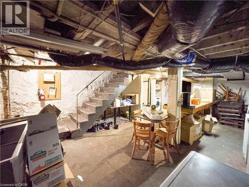 Utility basement featuring exposed stone foundation walls, concrete flooring, and an open staircase with a metal handrail - 85 King Street W, Kitchener, ON 