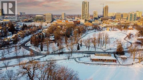 Expansive park area featuring snow-covered pathways and mature trees, surrounded by residential properties and a distant urban skyline - 85 King Street W, Kitchener, ON 