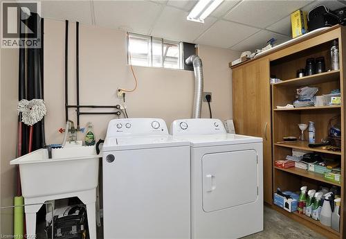 Dedicated utility space featuring a laundry sink, side-by-side washer and dryer, and built-in wood-finish shelving - 114 Bakersfield Drive, Cambridge, ON - Indoor Photo Showing Laundry Room