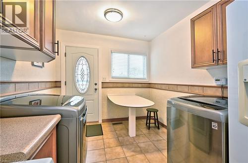 Utility room featuring tile flooring, a white paneled door with decorative glass, and a window with horizontal blinds - 1476 Barton Street E, Hamilton, ON - Indoor Photo Showing Laundry Room