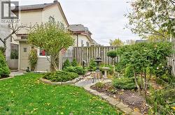 Private backyard featuring manicured lawn, established shrubbery, a paved pathway, a decorative fountain, and a wood privacy fence - 