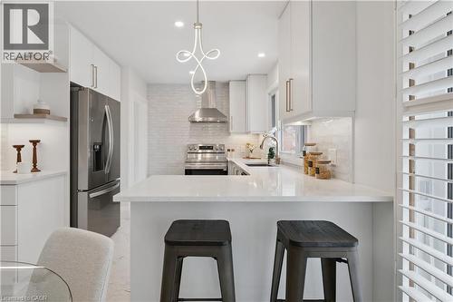 Modern kitchen featuring white cabinetry with brushed gold hardware, stainless steel appliances, a white tile backsplash, and a breakfast bar with white quartz countertops - 111 Ruskview Road, Kitchener, ON - Indoor Photo Showing Kitchen With Upgraded Kitchen