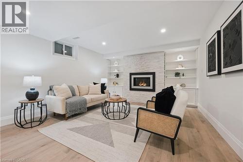 Recessed lighting illuminates this bright living space featuring light wood-finish flooring, a contemporary fireplace with a stone surround, and built-in shelving - 111 Ruskview Road, Kitchener, ON - Indoor Photo Showing Other Room With Fireplace