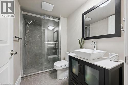 Modern bathroom featuring a sliding glass shower enclosure with gray stone-finish wall tile, a vessel sink on a white countertop, a dark wood-finish vanity with frosted glass doors, and a rectangular - 111 Ruskview Road, Kitchener, ON - Indoor Photo Showing Bathroom