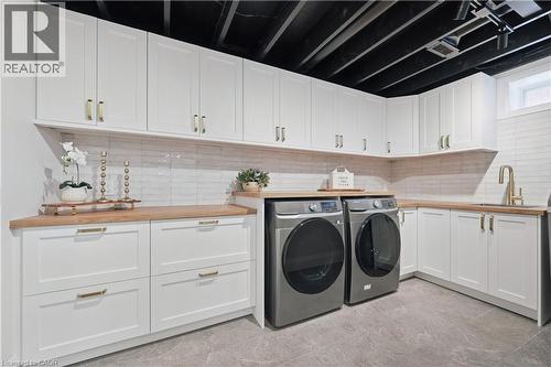 Laundry area featuring extensive white shaker cabinetry, wood-finish countertops, subway tile backsplash, a built-in sink with a gold-tone faucet, and stone-look tile flooring - 111 Ruskview Road, Kitchener, ON - Indoor Photo Showing Laundry Room
