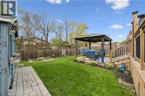 Expansive backyard featuring a manicured lawn, full privacy fencing, a wood-finish deck with a metal gazebo, and a paver stone pathway - 111 Ruskview Road, Kitchener, ON - Outdoor