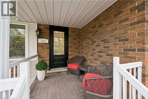 Covered front porch featuring a dark entry door with decorative glass, brick facade, white railing, wood-finish flooring, and a wall-mounted light fixture - 111 Ruskview Road, Kitchener, ON - Outdoor With Deck Patio Veranda With Exterior