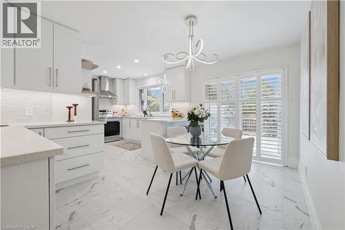 Modern kitchen featuring white cabinetry, light-toned countertops, a glass top dining table with seating for four, and white plantation shutters on the patio doors - 111 Ruskview Road, Kitchener, ON - Indoor Photo Showing Dining Room