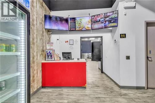 Reception area featuring a red service counter with a light-toned countertop, wood-finish accent wall, and wood-finish flooring - 545 Hespeler Road, Cambridge, ON 