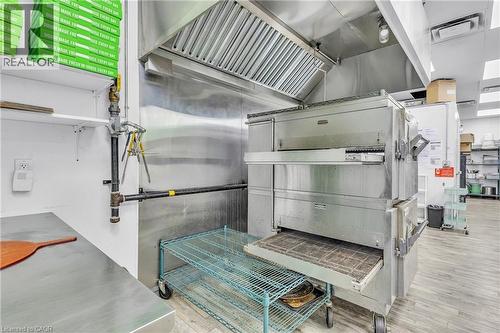 Commercial kitchen featuring stainless steel appliances, a large exhaust hood, metal shelving, and wood-finish flooring - 545 Hespeler Road, Cambridge, ON 