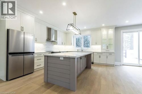 Dual tone kitchen featuring freestanding refrigerator, decorative backsplash, dual tone cabinets, light wood-type flooring, and a kitchen island - 1105 Main Street E, Cambridge, ON - Indoor Photo Showing Kitchen With Stainless Steel Kitchen With Upgraded Kitchen