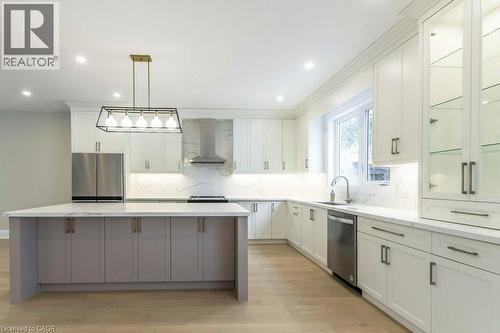 Dual tone kitchen featuring stainless steel appliances, light wood-type flooring, backsplash, light stone countertops, and a center island - 1105 Main Street E, Cambridge, ON - Indoor Photo Showing Kitchen With Upgraded Kitchen
